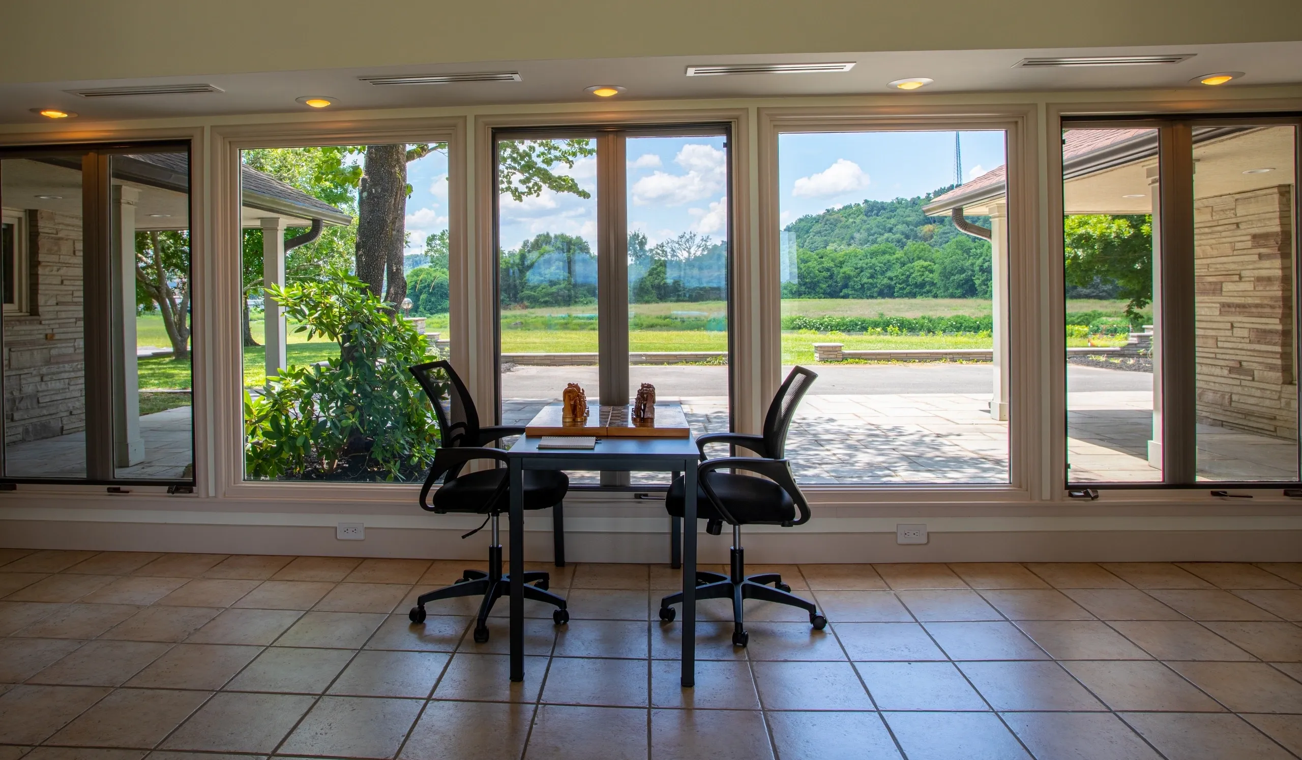 Table and chairs by large sunny windows.