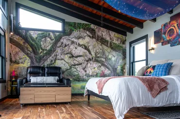 A bedroom with a bed, couch and wall mural.
